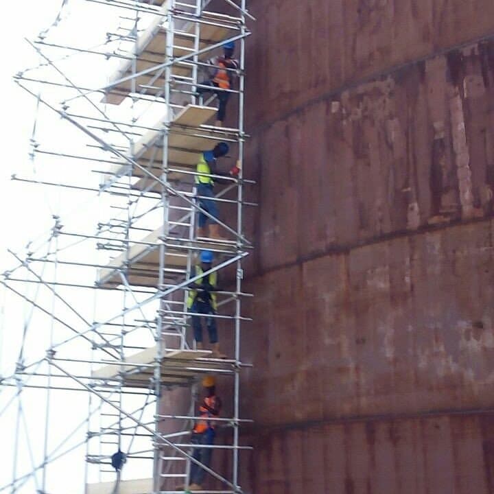 Workers in PPE ascending scaffolding alongside an industrial storage tank